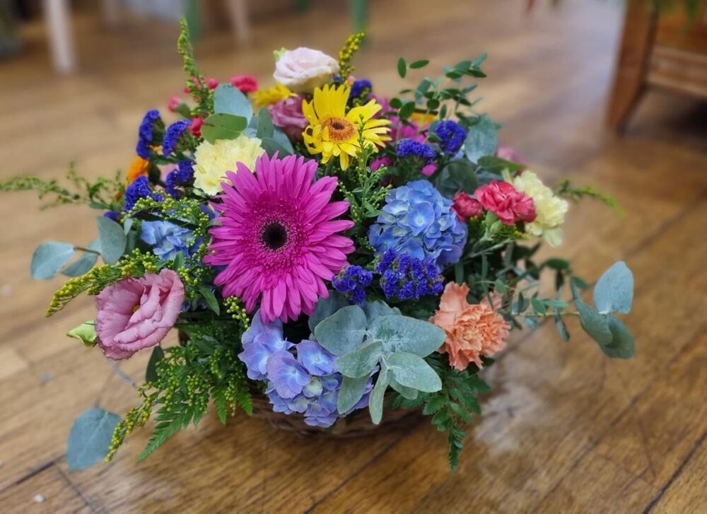 Composition florale multicolore de deuil avec gerberas fuchsia, hortensias bleus et feuillage – Pom'Violette