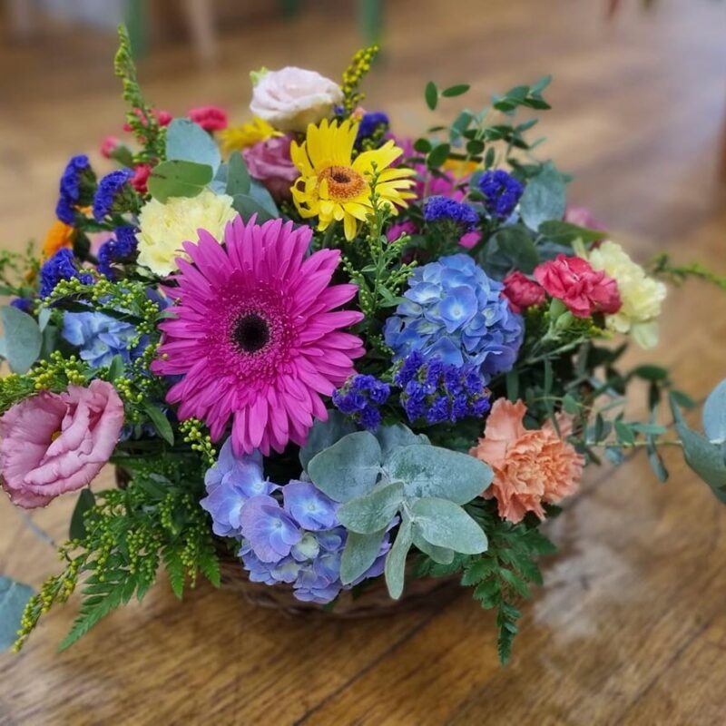 Composition florale multicolore de deuil avec gerberas fuchsia, hortensias bleus et feuillage – Pom'Violette